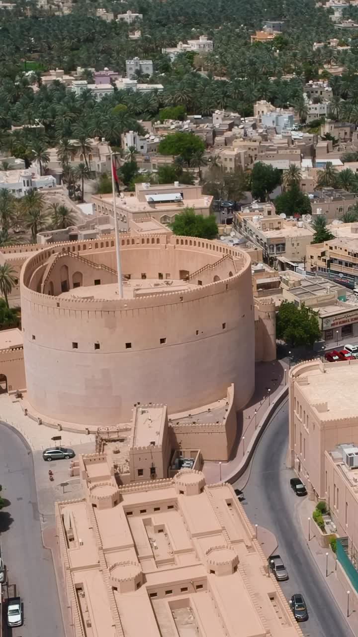 Vista aerea verticale con drone di Nizwa, con la fortezza storica, la torre e le mura nel Sultanato dell'Oman.