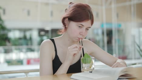 young woman reading a book and sipping a cocktail with a straw at a wooden counter in a bright, modern cafe with natural light. relaxed and focused ambiance