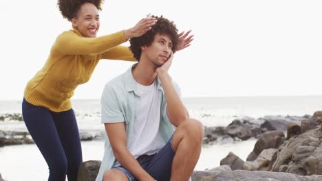 African-american-woman-closing-eyes-of-her-husband-from-behind-on-the-rocks-near-the-sea