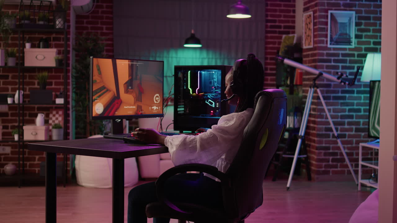 Over shoulder view of african american gamer girl using pc gaming setup playing multiplayer streaming online action game