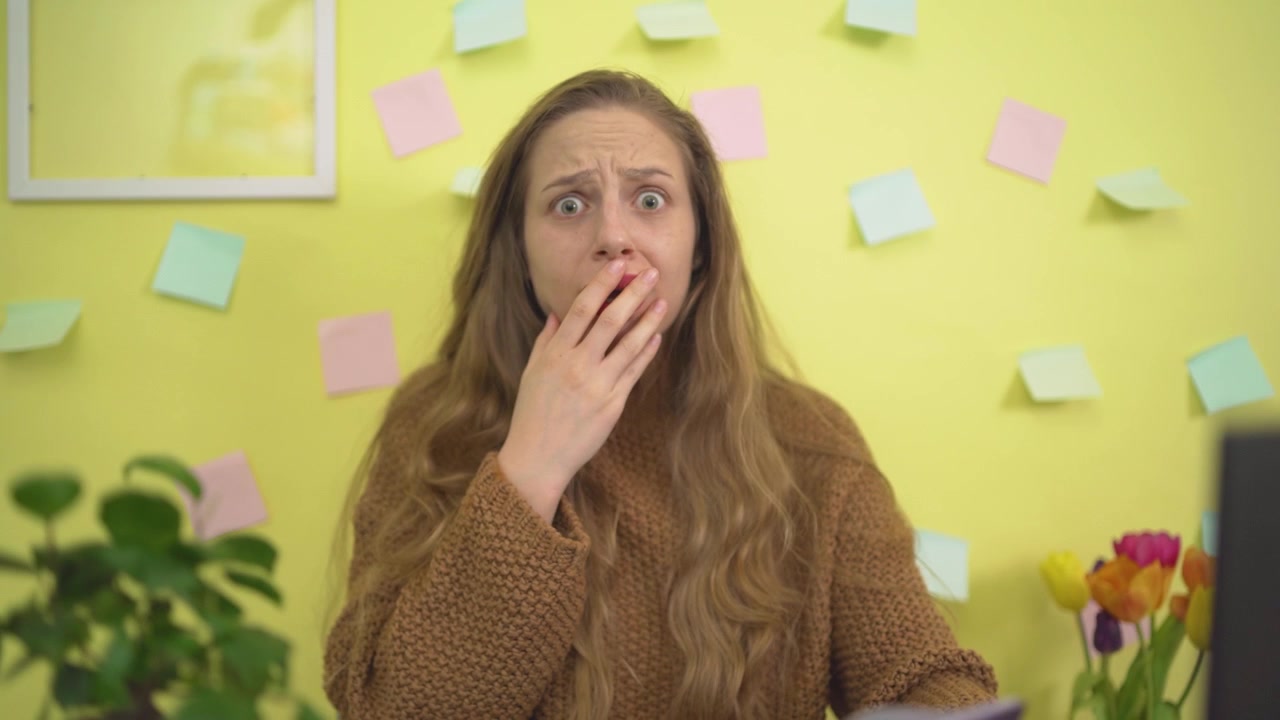 Una donna lavora al computer portatile alla sua scrivania e si copre la bocca per la sorpresa. Perfetto per concetti legati alla produttività, al lavoro da remoto o a notizie inaspettate