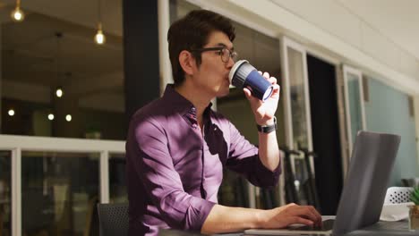 Asiatischer-Mann-Trinkt-Kaffee-Und-Benutzt-Laptop,-Während-Er-In-Einem-Café-Sitzt