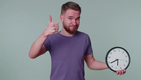 bearded young man showing time on clock watch, ok, thumb up, approve, pointing finger at camera