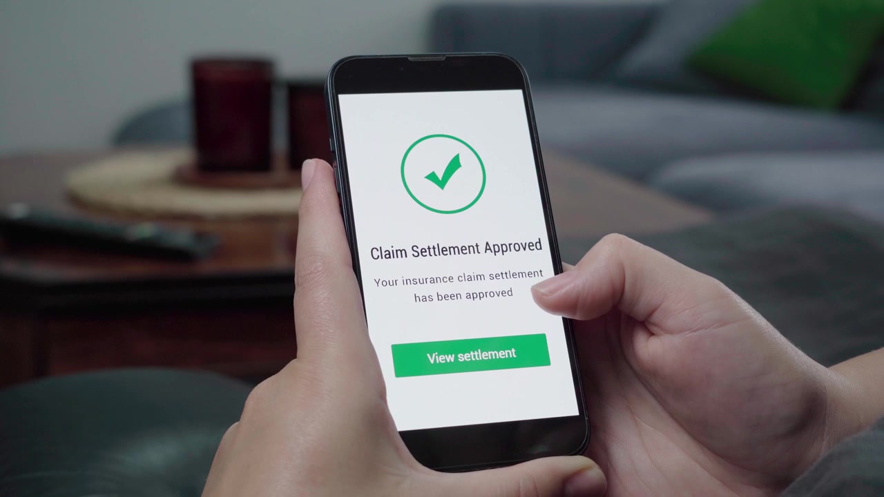 Mani che tengono uno smartphone che mostra un messaggio "Liquidazione del sinistro approvata" con un segno di spunta verde e un pulsante "Visualizza liquidazione"