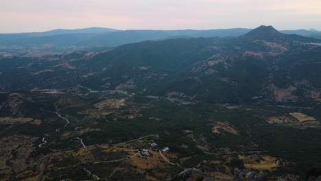 A-drone-rises-above-the-stone-peaks-of-a-mountain,-revealing-a-wide-valley