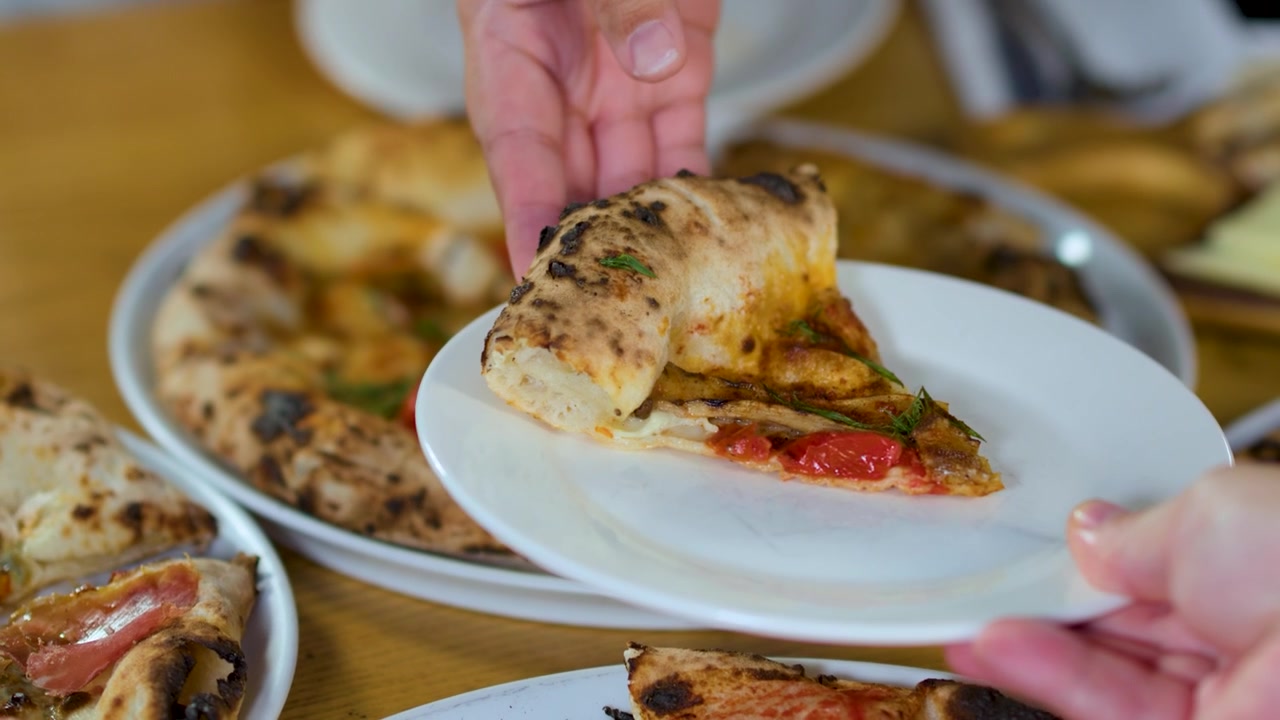 Primo piano di una mano che serve una fetta di pizza gourmet su un piatto di ceramica bianco