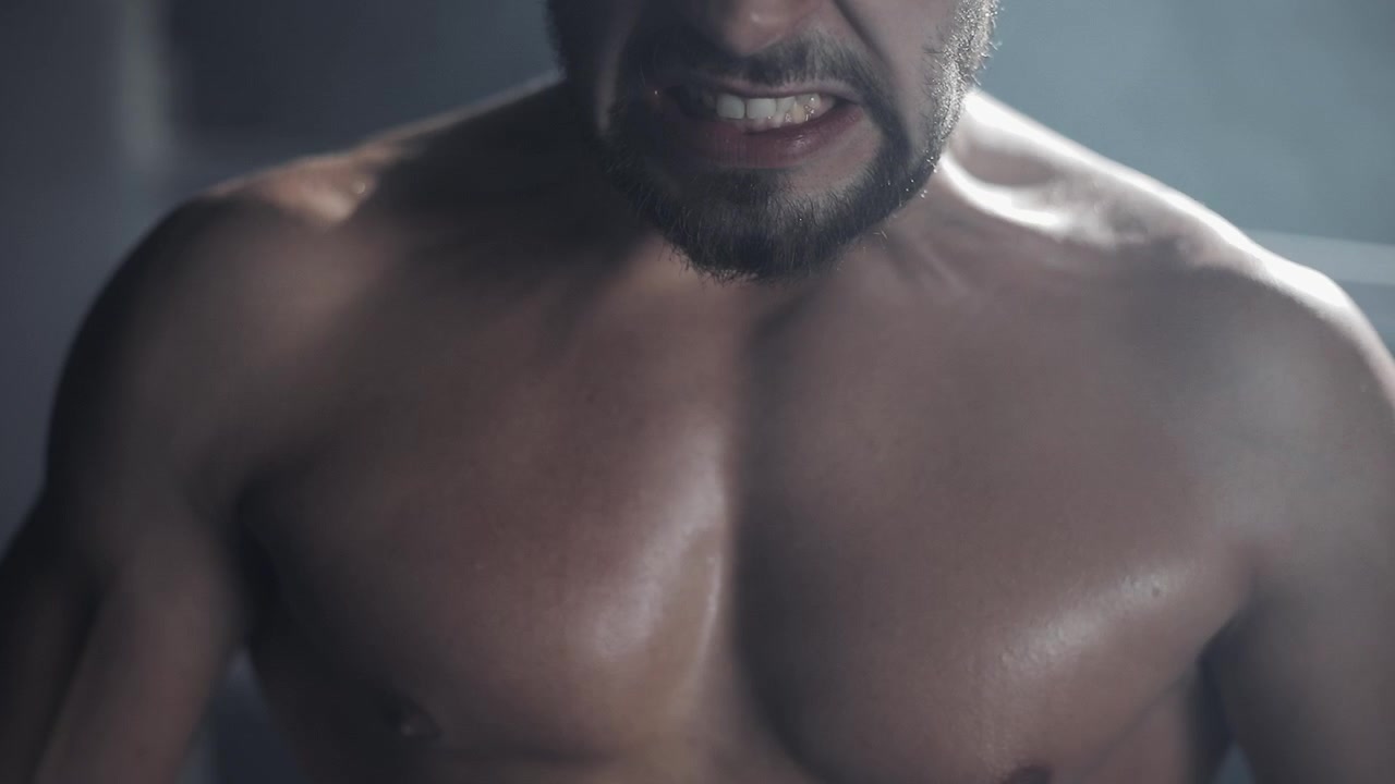 Uomo muscoloso che respira affannosamente e stringe i denti durante un allenamento intenso.