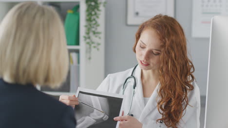 female doctor or consultant wearing white coat having meeting with female patient to discuss scans