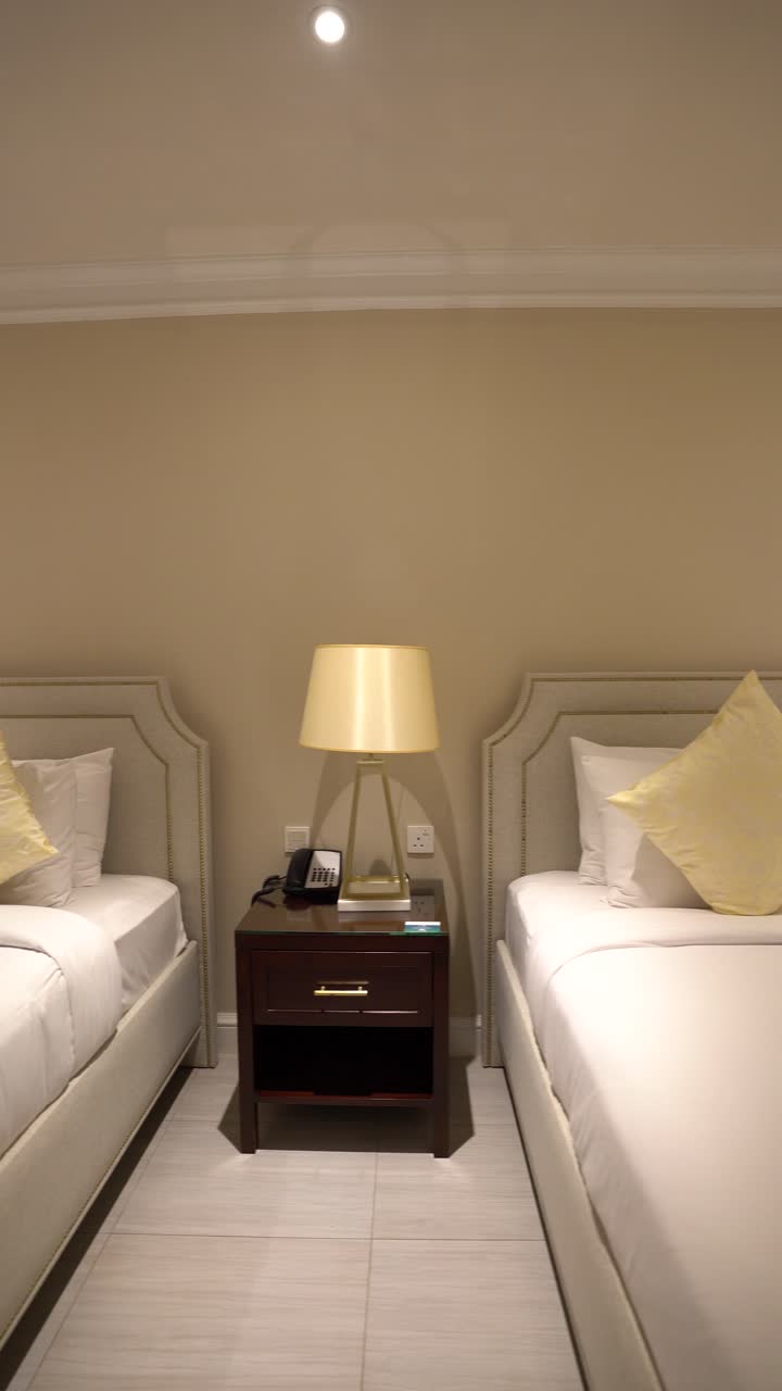 Clean and comfortable hotel room featuring two single beds with white linens, a yellow accent pillow, and a bedside lamp. Perfect for travel concepts
