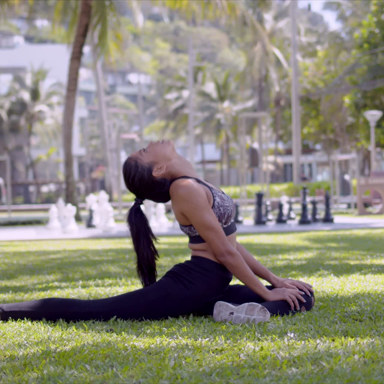 Mulher asiática esbelta alongando o pescoço e as pernas sentada no parque