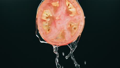 agua que fluye por rodaja de tomate fresco con goteo líquido en cámara lenta con fondo negro retroiluminado