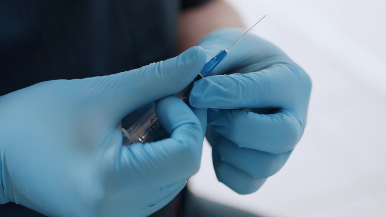 Preparazione medica precisa. Un'infermiera attenta prepara un'iniezione con guanti e strumenti sterili. Il professionista sanitario assembla con cura la siringa dall'ampolla con precisione e attenzione