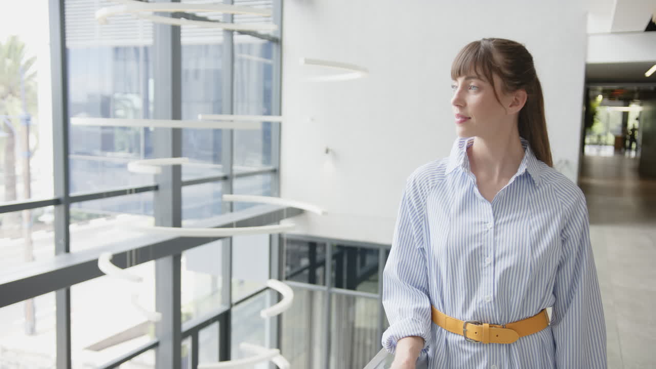 Standing in modern office, woman in striped shirt looking at camera, copy space