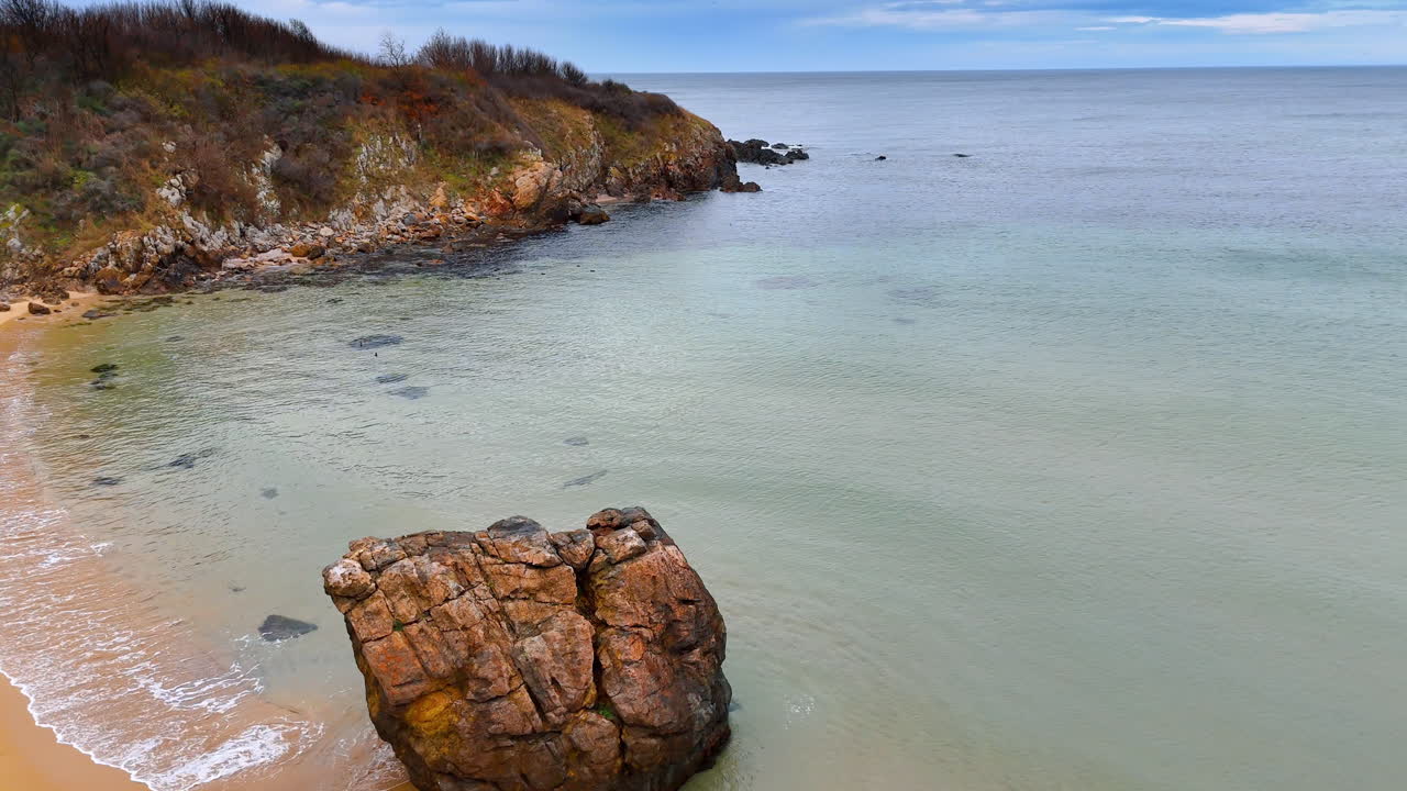 Baia con spiaggia sabbiosa e grande roccia in acqua. Ampia inquadratura di una spiaggia sabbiosa appartata con un enorme masso sulla riva e mare calmo.