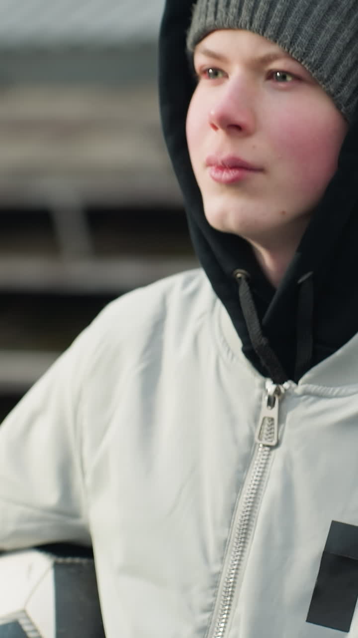 Close-up of a young boy wearing a gray sweater, holding a soccer ball under his arm while looking focused