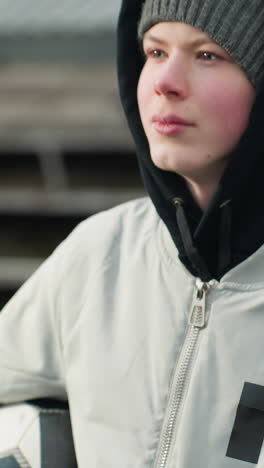 close-up of a young boy wearing a gray sweater, holding a soccer ball under his arm while looking focused
