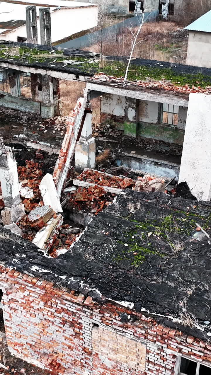 Fully ruined building with no roof or windows. Scattered bricks, beams and pieces of concrete from a premise after armed conflict. Aerial view. Vertical video