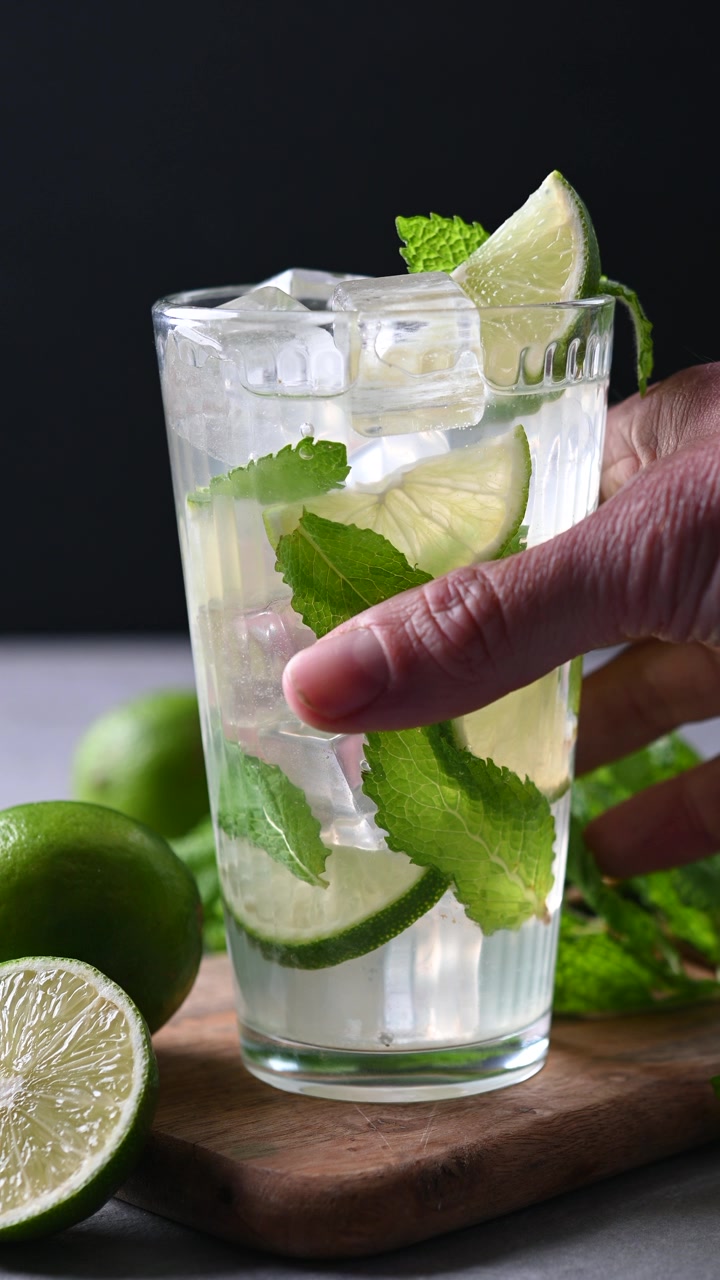 Mano che prende un cocktail mojito da un tavolo con menta fresca e lime