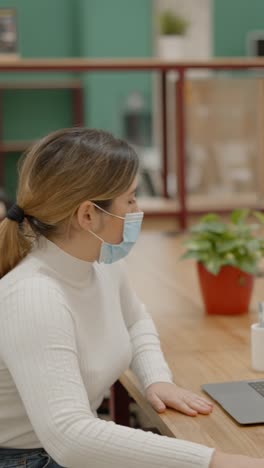woman in face mask working on laptop in an office