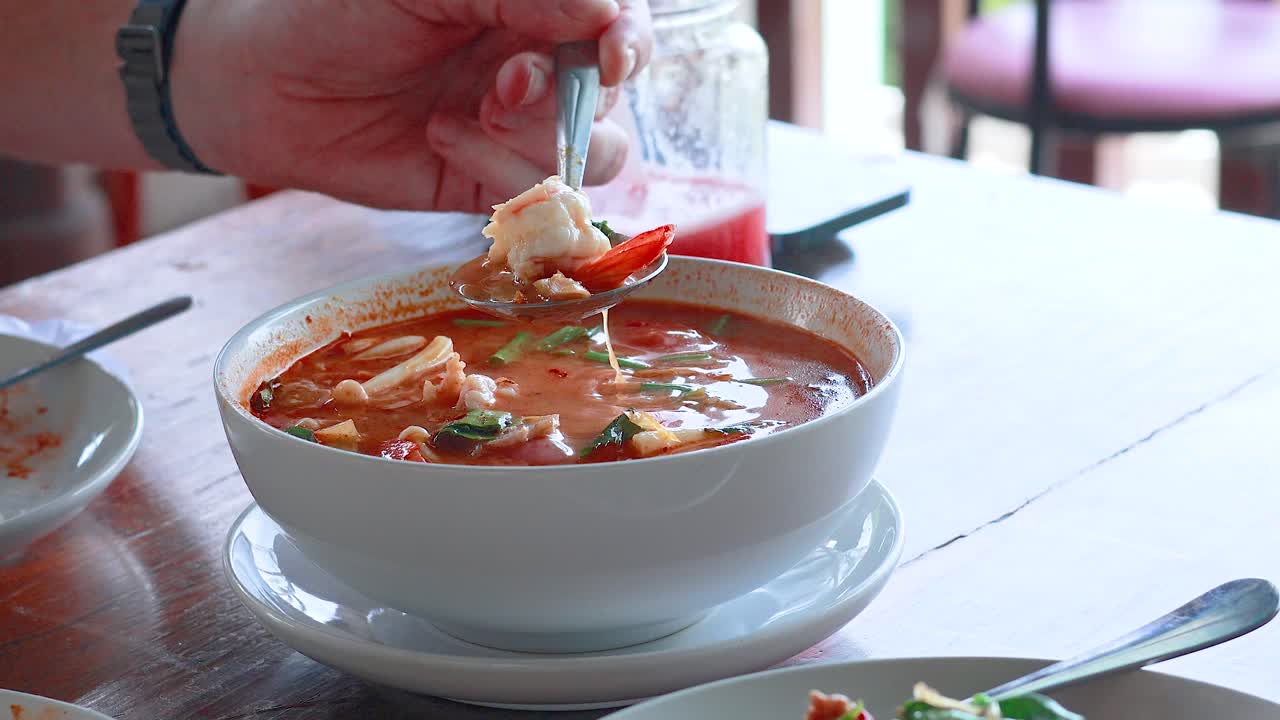 A person savors Tom Yum Kung soup, capturing the vibrant flavors and textures in a bright, inviting setting