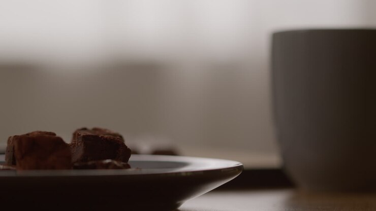 Close Up Of Plate Of Chocolate Brownies Next To Person Drinking Hot Drink From Mug