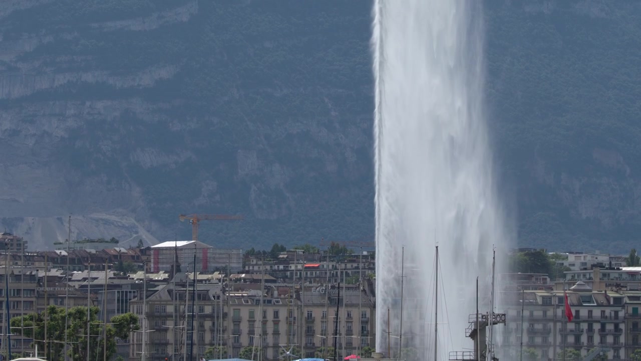 Statische Weitwinkelaufnahme einer riesigen vertikalen Wasserfontäne vor einer europäischen Stadtsilhouette.