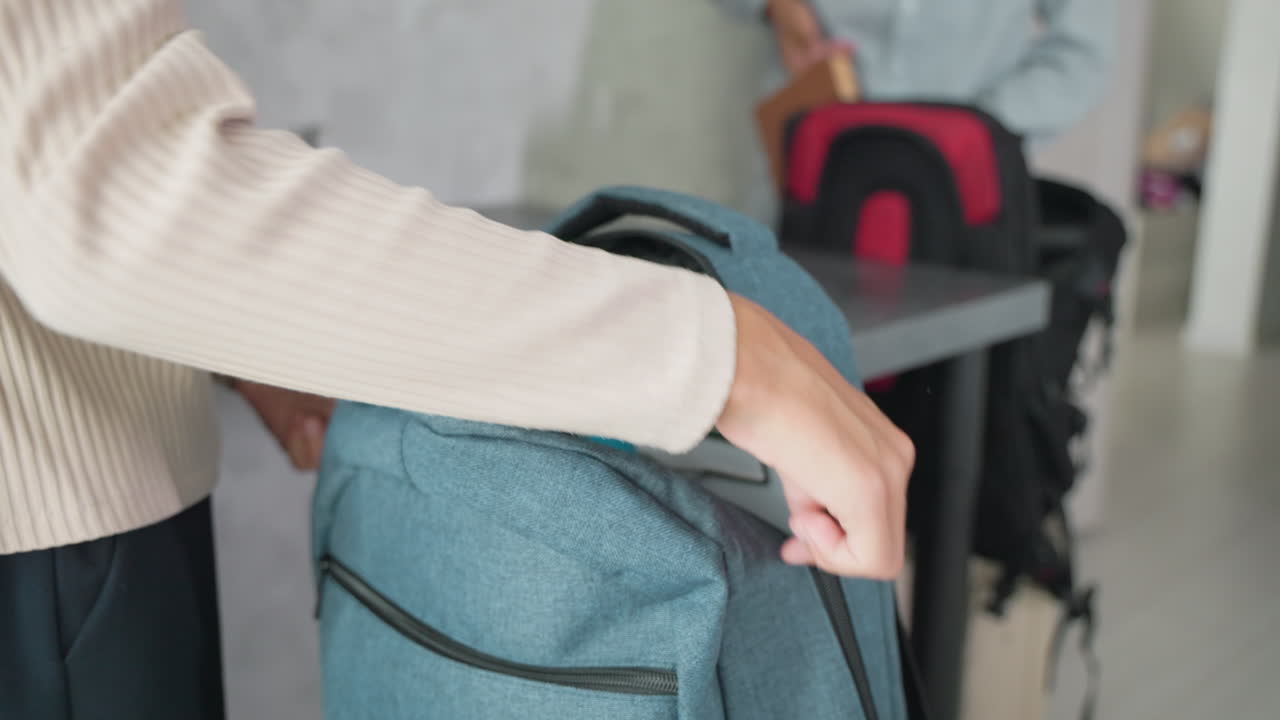 girl and boy in casual wear packing backpacks on kitchen counter placing notebooks water bottles lunch boxes ready for school routine morning preparation with organization and sibling teamwork