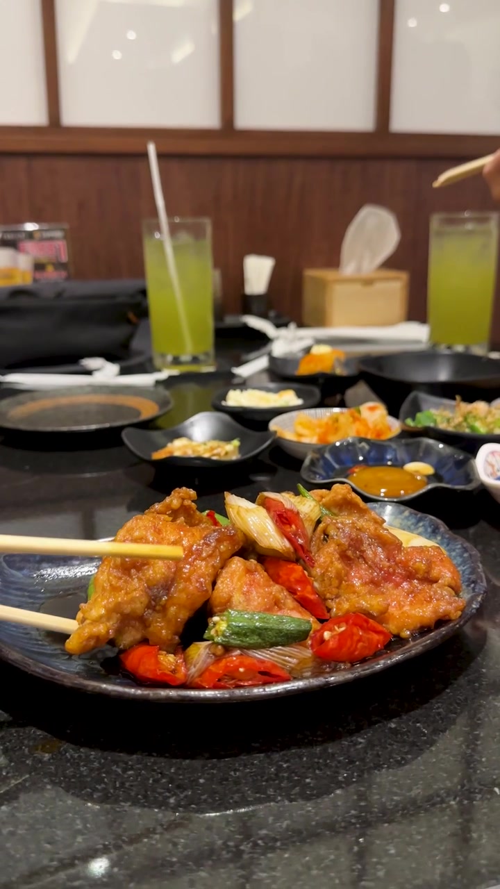 Close-up of chopsticks lifting crispy fried chicken from a plate in a Bangkok restaurant.