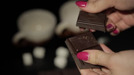 woman breaks black chocolate bar. close-up. slow motion