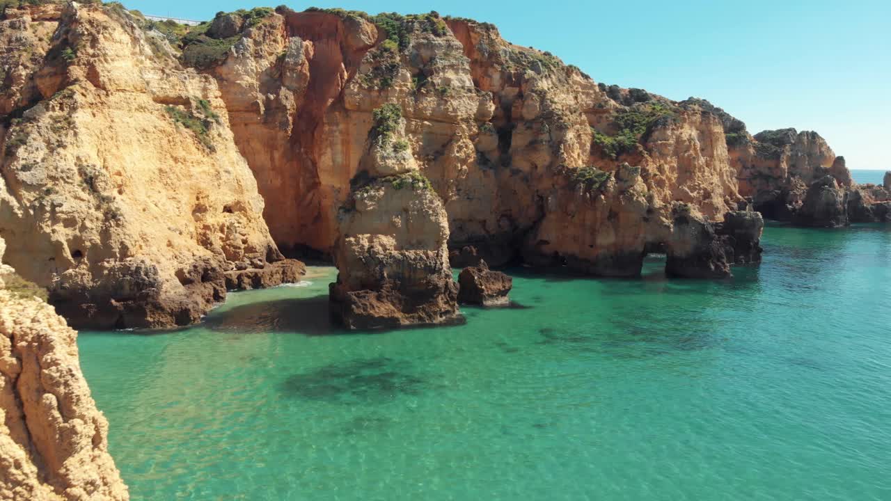 Craggy cliffs jutting out of crystal clear waters of the Algarve Sea, in Lagos, Portugal - Aerial ground level Fly-over shot
