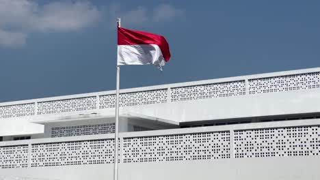 movimiento lento de la bandera roja y blanca de la bandera indonesia revoloteando frente al edificio blanco bajo el cielo azul