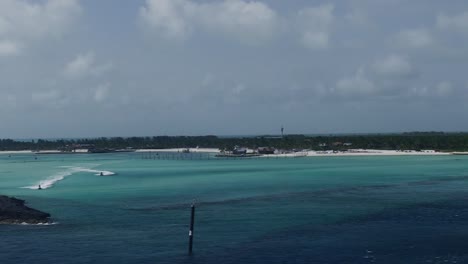 Cruise-Ship-pulling-away-from-Cay-in-Bahamas,-Two-jet-skis-race-by