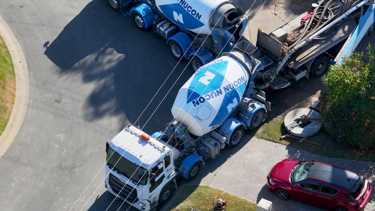 Concrete mixer truck pours concrete at suburban construction site, aerial view, bright daylight, minimal movement