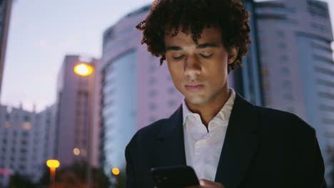 Hombre-De-Negocios-Preocupado-Leyendo-Un-Teléfono-Inteligente-En-La-Calle-Nocturna.-Joven-Mirando-La-Pantalla