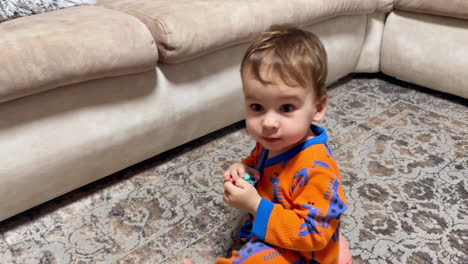 little baby in orange romper with giraffes crawls by the floor. happy kid finds the pacifier and gives it to somebody.