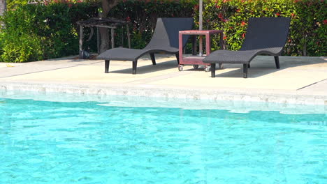 two empty beach loungers sit along the edge of a resort pool
