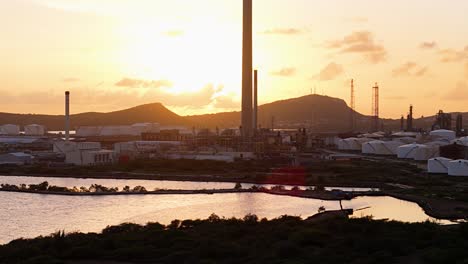 large petroleum tanks of fuel and flare stacks backlit by sunset in curacao