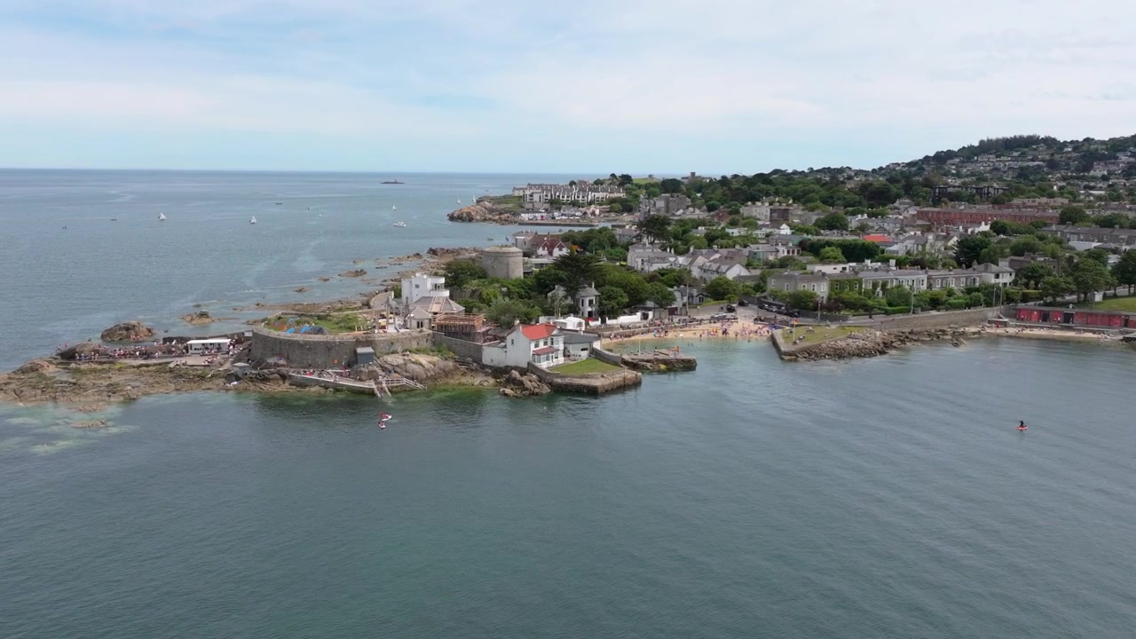 Survol aérien lent révélant la crique de baignade Forty Foot, la tour Martello et le littoral suburbain environnant par une calme journée d'été