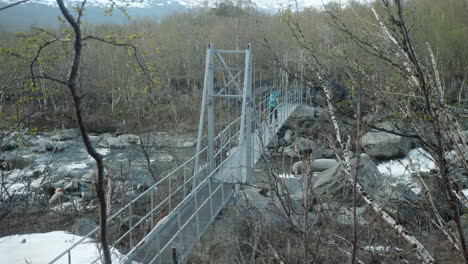 blond female hiker walking over a suspension bridge on the kungsleden in the swedish mountains, backpacking in the forest