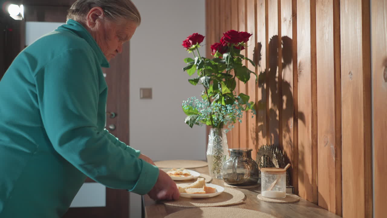 Elderly woman carrying two plates with bread slices, preparing breakfast in cozy kitchen with wooden walls and fresh flowers on table. Morning routine, serving meal, home cooking concept