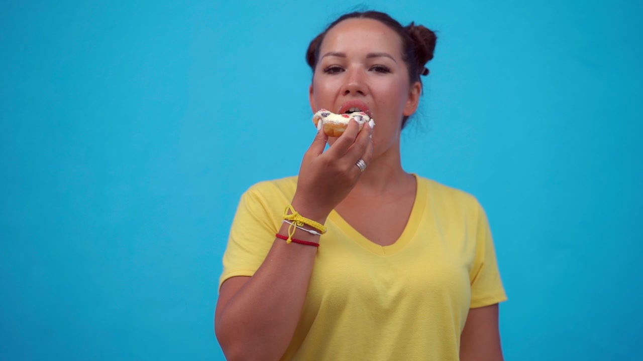 Young Woman Eating a Glazed Donut Against a Blue Background
