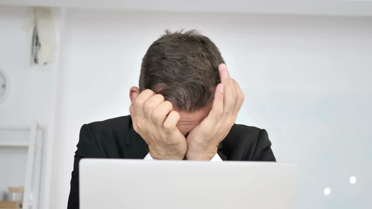 Tired Businessman Rubbing Eyes while Working on Laptop