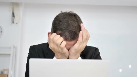 tired businessman rubbing eyes while working on laptop