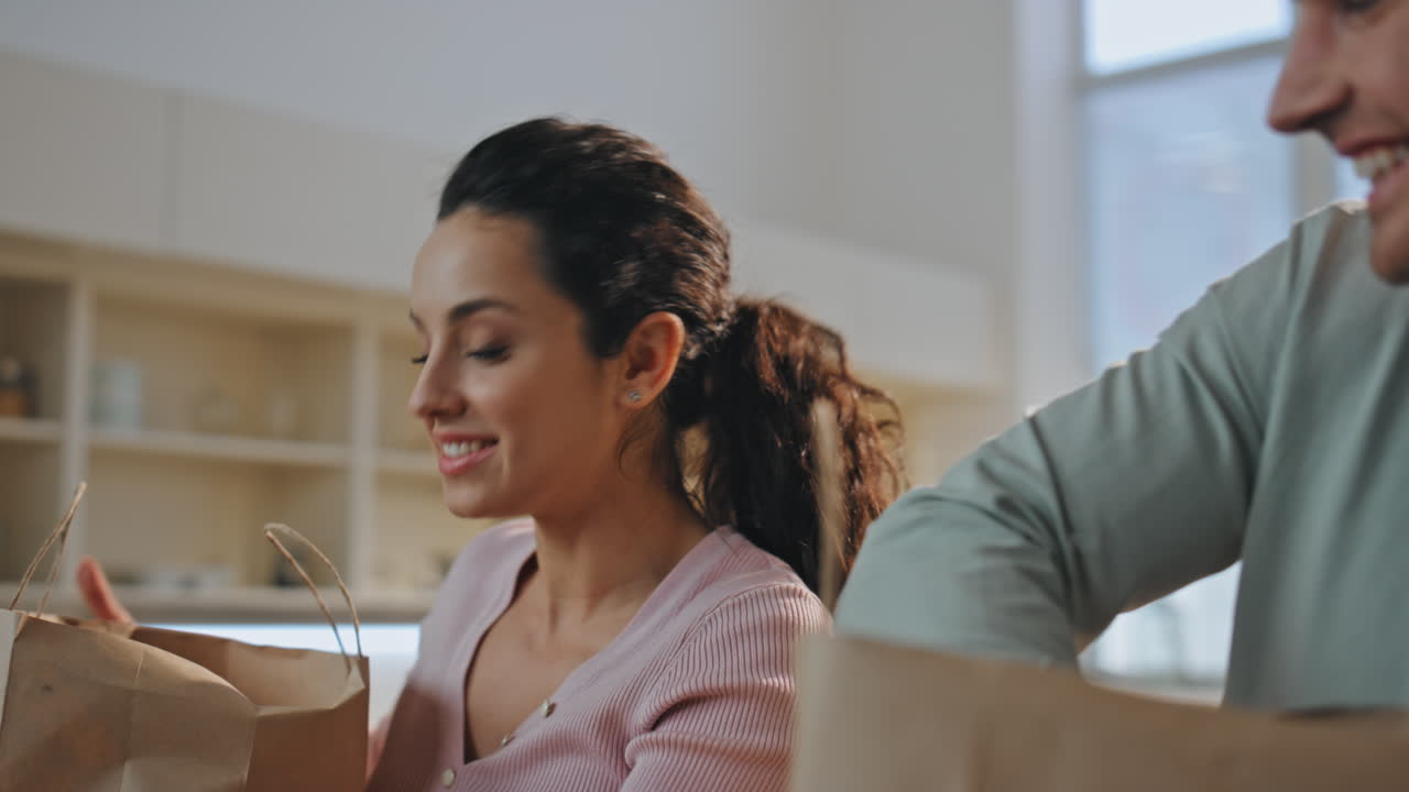 Spouses taking out products from paper package at kitchen. Family unpacking food