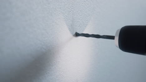 young male handyman using cordless screwdriver to mount a wooden magazine holder on a white wall with a srew at home detail close up 4k