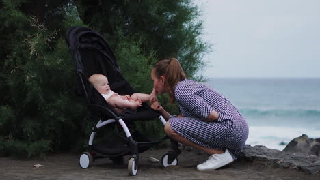 an affectionate and caring young mother interacts with her baby in the stroller, creating a heartwarming scene for this sweet young family against the ocean backdrop