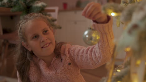 little girl decorates the christmas tree with balls at home