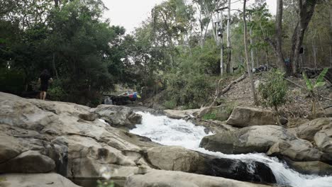 a person walks by a rocky river in a lush, forested landscape