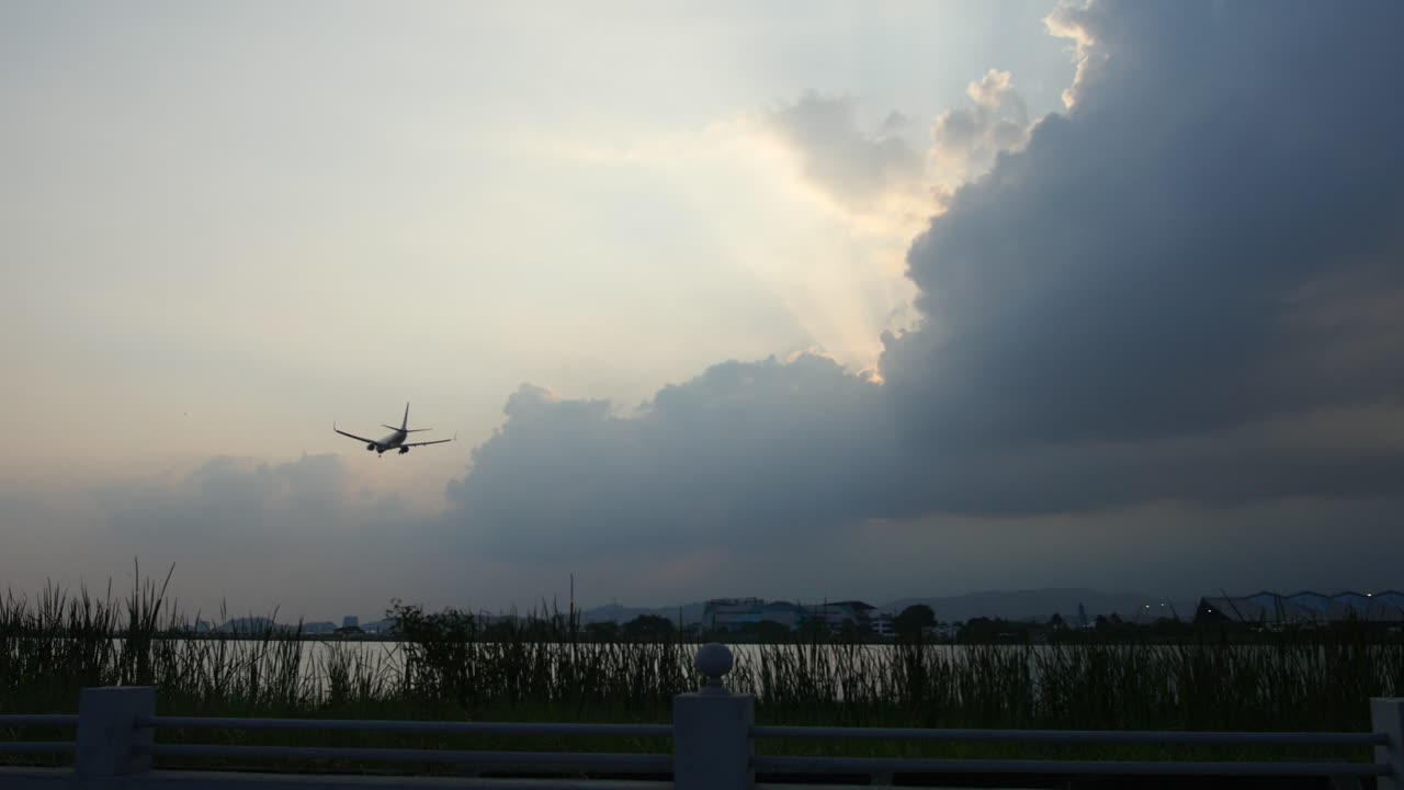 A commercial airplane approaches the airport for landing, gliding smoothly through the sky. The shot is taken from the riverbank,