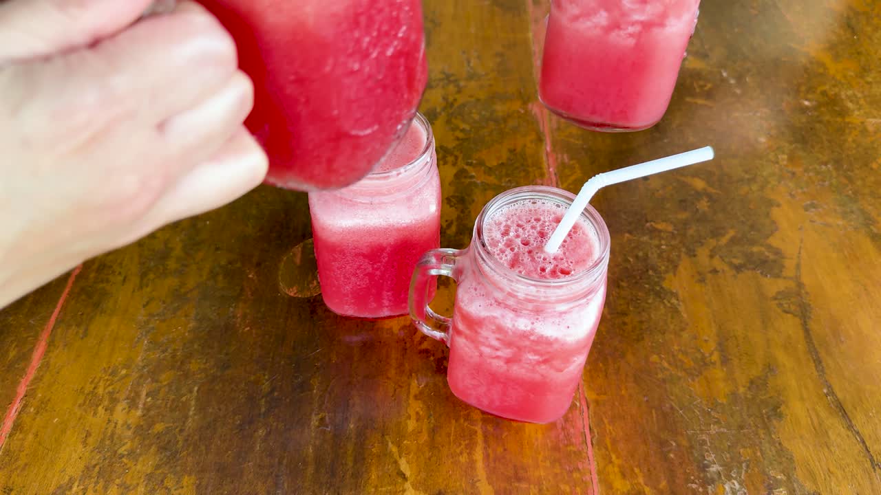 Due vivaci cocktail rosa in barattoli di vetro con cannucce su un tavolo di legno, catturati con luce naturale in un ristorante a Phuket.